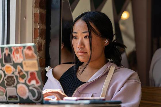 A student sits at a cafe table with a laptop